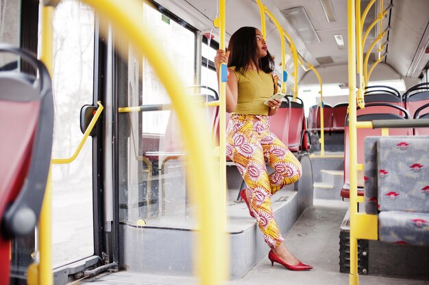 Młoda stylowa afroamerykanka jedzie autobusem z telefonem komórkowym