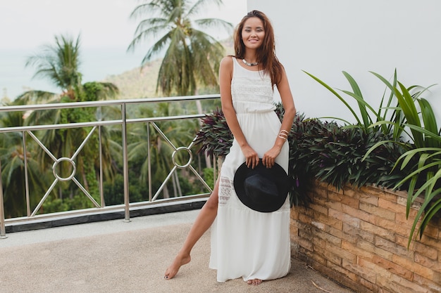 Bezpłatne zdjęcie młoda stylowa azjatka w białej sukni boho, styl vintage, naturalny, uśmiechnięty, szczęśliwy, tropikalne wakacje, hotel, palmy w tle