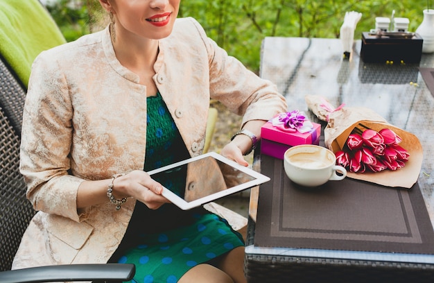 Młoda stylowa szczęśliwa kobieta siedzi w kawiarni, trzymając tablet