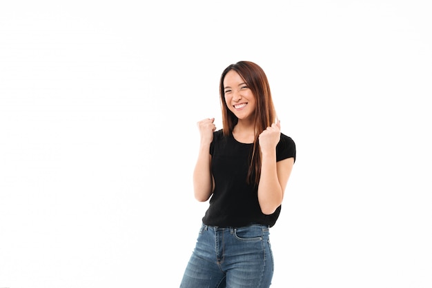 Młoda szczęśliwa azjatykcia dziewczyna w przypadkowej odzieży pokazuje zwycięzcy gest, patrzeje kamerę