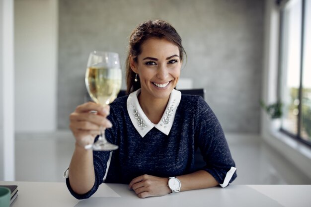 Młoda szczęśliwa bizneswoman wznosząca toast winem w biurze
