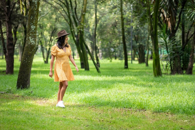Młoda szczęśliwa kobieta hiszpanie spacerując po parku ubrana w żółtą sukienkę i kapelusz.