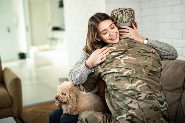 Młoda szczęśliwa kobieta obejmująca swojego wojskowego męża, który wrócił do domu z wojny