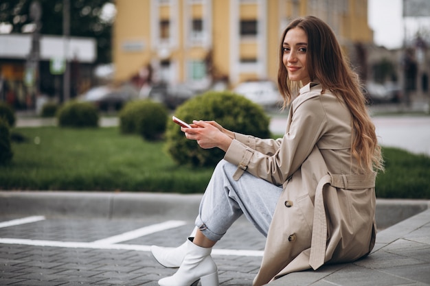 Bezpłatne zdjęcie młoda szczęśliwa kobieta siedzi w parku i rozmawia przez telefon