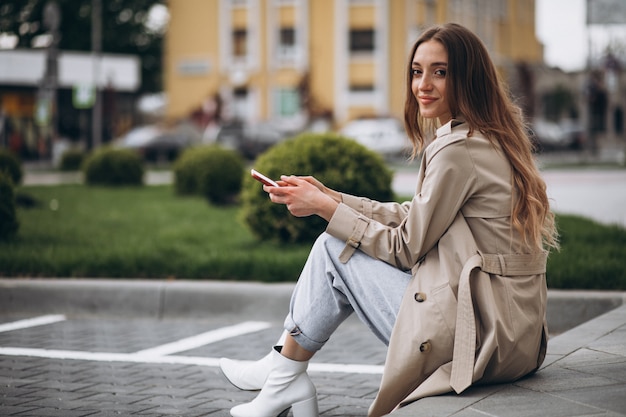Młoda szczęśliwa kobieta siedzi w parku i rozmawia przez telefon