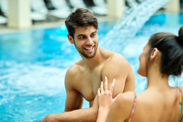 Młoda szczęśliwa para komunikująca się podczas relaksu przy basenie w spa Skupiamy się na człowieku