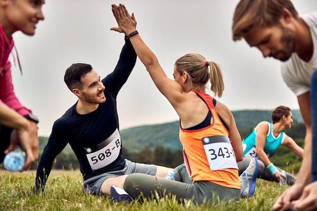 Bezpłatne zdjęcie młoda szczęśliwa para przybija sobie piątkę, rozciągając się na trawie przed biegiem maratonu