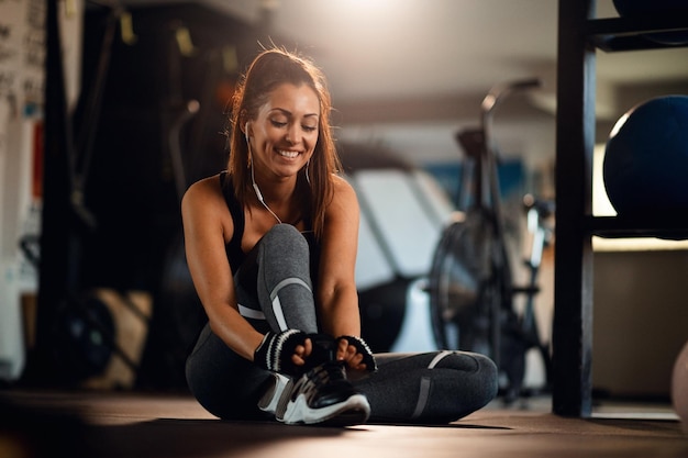 Młoda szczęśliwa sportsmenka przygotowuje się do treningu i wiązania sznurowadła w centrum fitness