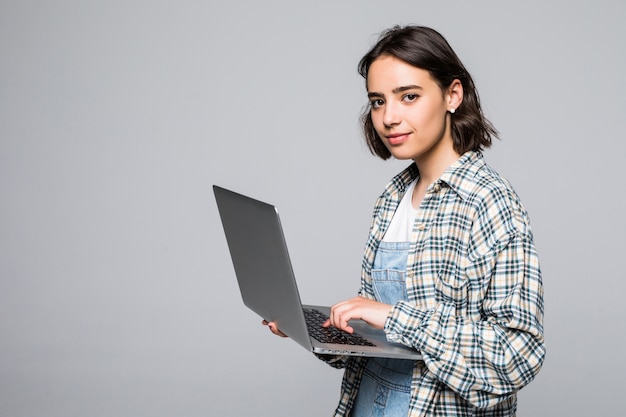 Młoda Szczęśliwa Uśmiechnięta Kobieta W Ubranie Trzyma Laptopa I Wysyła E-mail Do Swojego Najlepszego Przyjaciela Na Szarym Tle