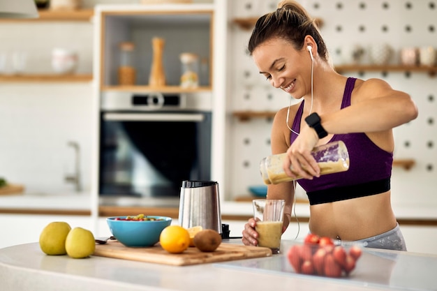 Młoda, szczęśliwa, wysportowana kobieta ma koktajl owocowy na śniadanie w kuchni
