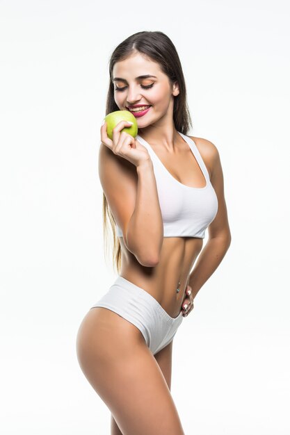 Młoda szczupła kobieta trzyma zielone jabłko. Na białym tle na białej ścianie. Pojęcie zdrowej żywności a kontrola nadwagi.