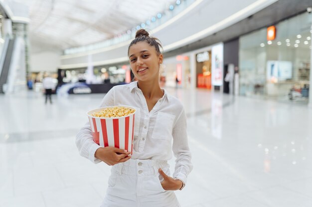 Młoda urocza kobieta trzyma popcorn w tle centrum handlowego