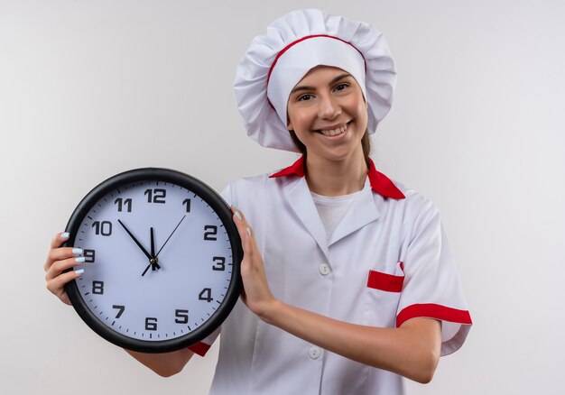 Młoda uśmiechnięta dziewczyna kaukaski kucharz w mundurze szefa kuchni trzyma zegar na białym z miejsca na kopię