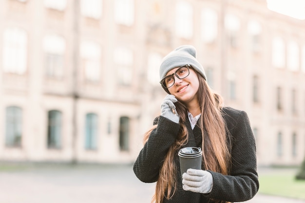 Bezpłatne zdjęcie młoda uśmiechnięta kobieta opowiada na smartphone na ulicie z filiżanką