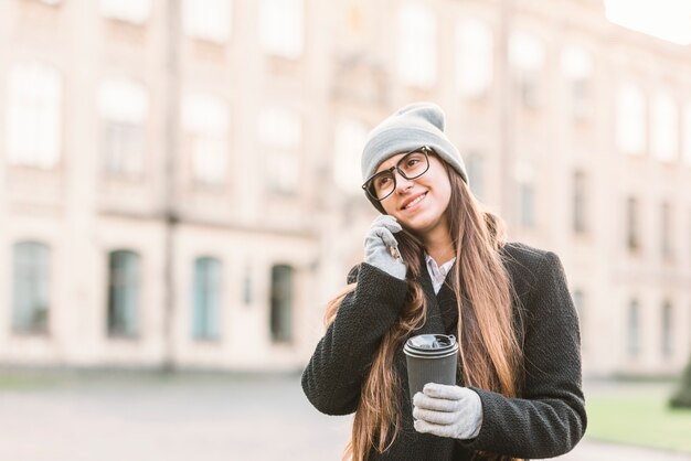 Młoda uśmiechnięta kobieta opowiada na smartphone na ulicie z filiżanką