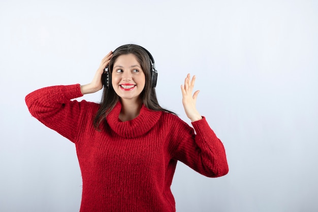 Młoda uśmiechnięta kobieta w czerwonym ciepłym swetrze stojąca ze słuchawkami