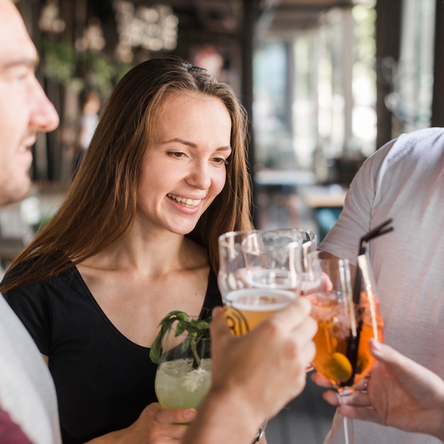 Młoda uśmiechnięta kobieta wznosi toast napoje z jej przyjaciółmi