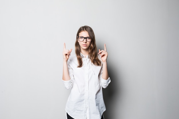 Młoda uśmiechnięta ładna dziewczyna w okularach ubrana w ścisłe biuro biała koszulka stoi przed białą ścianą