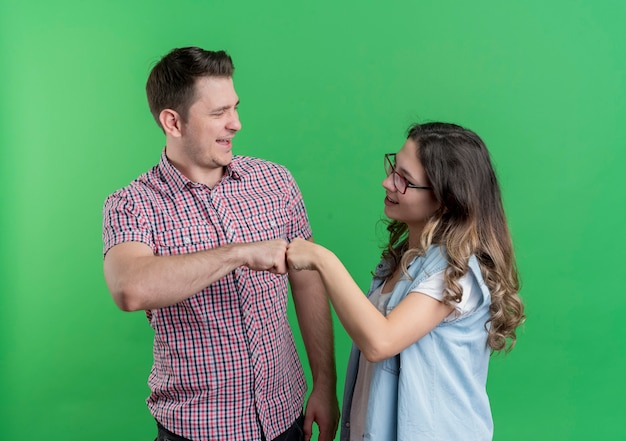 Bezpłatne zdjęcie młoda wesoła para mężczyzna i kobieta, dając uderzenie pięścią patrząc na siebie, dokonywanie transakcji na zielono