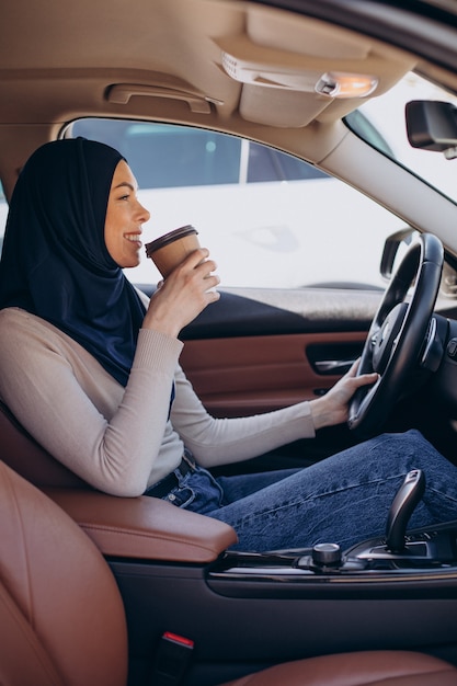 Młoda współczesna muzułmanka pije kawę w samochodzie