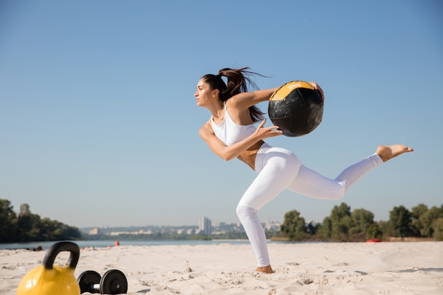 Młoda zdrowa kobieta działa z piłką na plaży.