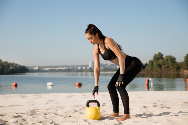 Młoda zdrowa kobieta robi przysiady z ciężarami na plaży.