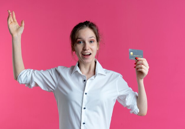 młoda zdziwiona blondynka Rosjanka trzyma kartę kredytową i podnosi rękę