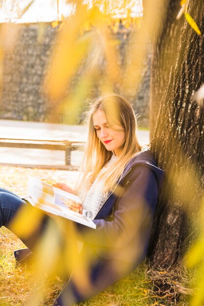 Młoda żeńska czytelnicza książka opiera jesieni drzewa