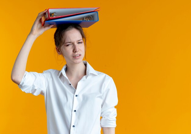 Młoda zirytowana blondynka Rosjanka trzyma foldery plików nad głową na pomarańczowej przestrzeni z miejsca na kopię