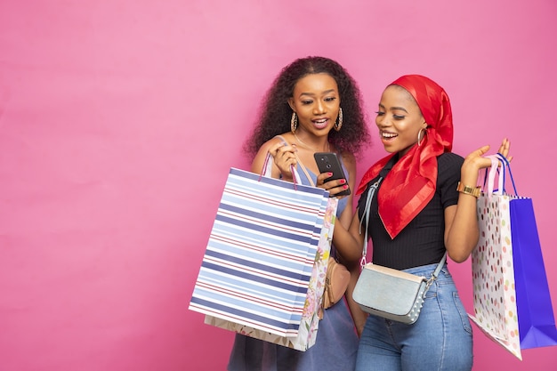 Młode afrykańskie panie oglądają coś na telefonie komórkowym, niosąc torby z zakupami