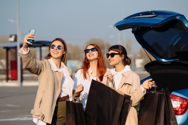 Młode kobiety w samochodzie z torby na zakupy. Dziewczyny robią selfie