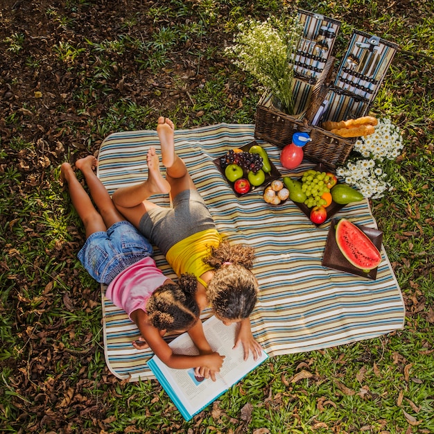 Młode siostry czyta na ściereczkach piknikowych