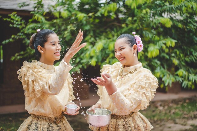 Młode uśmiechnięte kobiety ubierają się w piękne tajskie kostiumy, rozpryskując wodę w świątyniach i zachowują dobrą kulturę Tajów podczas festiwalu Songkran podczas kwietniowego tajlandzkiego Nowego Roku.