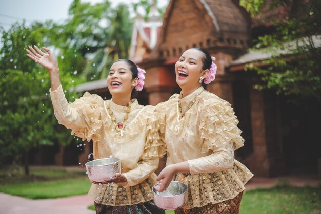Młode uśmiechnięte kobiety ubierają się w piękne tajskie kostiumy, rozpryskując wodę w świątyniach i zachowują dobrą kulturę Tajów podczas festiwalu Songkran podczas kwietniowego tajlandzkiego Nowego Roku.