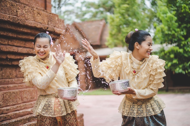 Bezpłatne zdjęcie młode uśmiechnięte kobiety ubierają się w piękne tajskie kostiumy, rozpryskując wodę w świątyniach i zachowują dobrą kulturę tajów podczas festiwalu songkran podczas kwietniowego tajlandzkiego nowego roku.