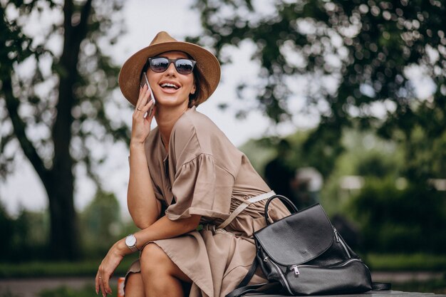 Bezpłatne zdjęcie młodej kobiety obsiadania park używać telefon