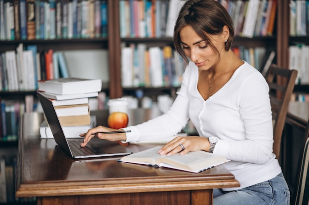 Młodej kobiety obsiadanie przy biblioteką używać książki i komputer