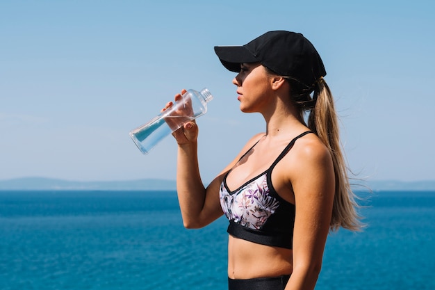 Młodej kobiety pozycja przed błękitną denną wodą pitną od butelki