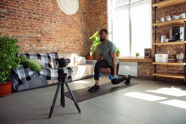 Młody Afroamerykanin nauczający w domu online kursy fitness, aerobik, sportowy styl życia podczas kwarantanny, nagrywanie przed kamerą, streaming