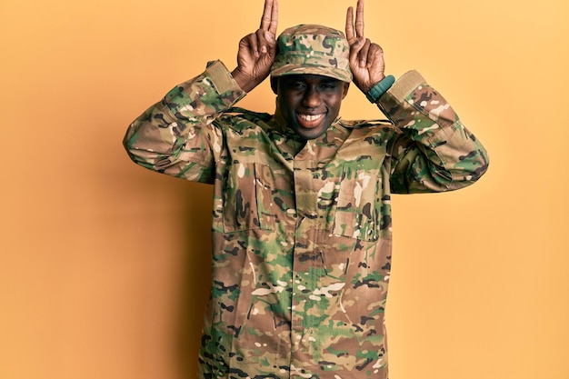 Bezpłatne zdjęcie młody afroamerykanin w mundurze wojskowym, pozujący zabawnie i szalony z palcami na głowie jak uszy królika, uśmiechając się wesoło