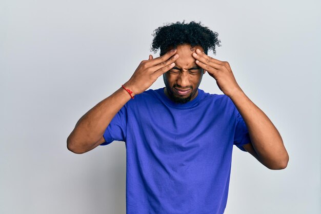 Młody afroamerykanin z brodą, ubrany w swobodną niebieską koszulkę z ręką na głowie, ból głowy z powodu stresu. cierpiący na migrenę.