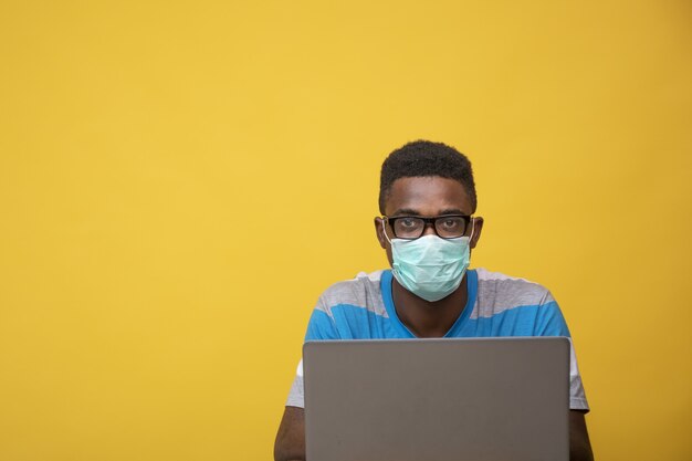 Młody Afrykanin w okularach i masce podczas pracy na laptopie – COVID-19