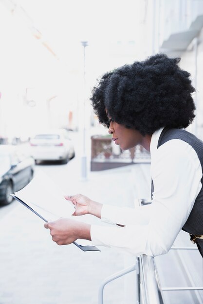 Młody afrykański bizneswoman opiera na poręcza czytającym dokumencie na papierze