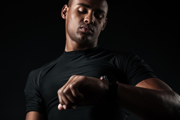 Młody afrykański mięśniowy mężczyzna patrzeje zegarek