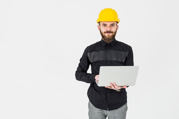 Młody architekt jest ubranym żółtego hardhat mienia przenośnego laptop