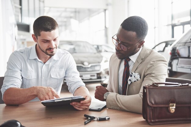 Młody atrakcyjny czarny biznesmen kupuje nowy samochód, podpisuje umowę i zabiera klucze do kierownika.