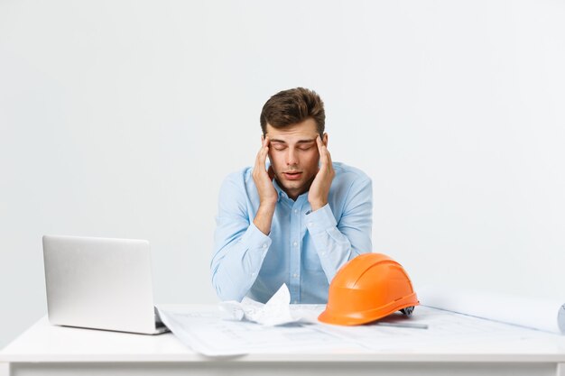 Młody atrakcyjny inżynier człowiek czuje się zmęczony w miejscu pracy.