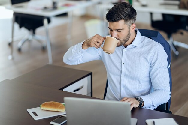 Młody biznesmen pije kawę podczas pracy na laptopie w biurze