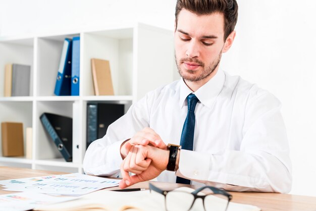 Młody biznesmen w miejscu pracy ogląda czas na zegarek na rękę