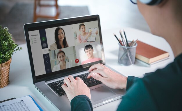 Młody biznesmen z Azji nosi słuchawki pracujące zdalnie z domu i wirtualne spotkanie wideokonferencyjne z kolegami z biznesu. pojęcie dystansu społecznego w domowym biurze.